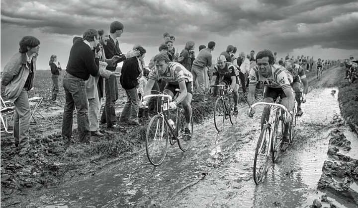 Cyclists fighting through a muddy Belgian race watched by roadside crowds