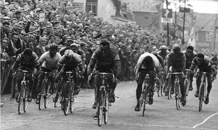 Racing cyclists climbing through a packed roadside crowd
